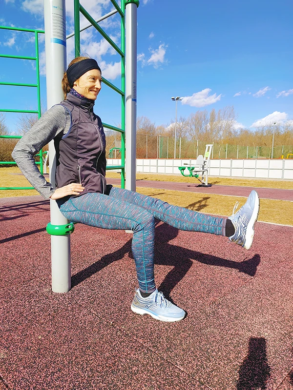 Ursula trainiert in einem öffentlichen Calisthenics-Park. Sie führt den Wandsitz an einer Stange aus und hebt abwechselnd eine Bein.