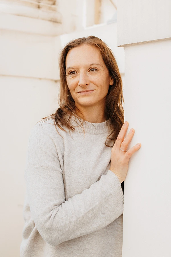 Portrait Ursula, Blick in die Ferne, stützt sich leicht mit der Hand an der Hausmauser ab